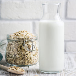 a glass carafe of oat milk next to a glass jar of oats