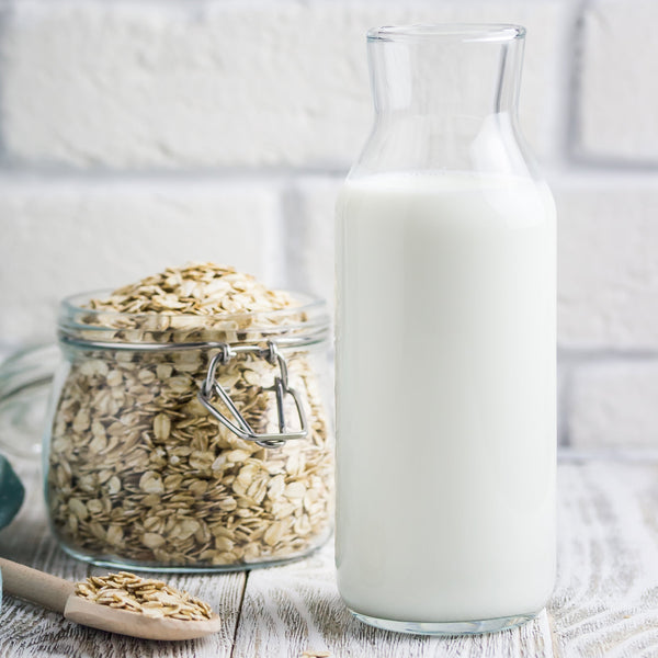 a glass carafe of oat milk next to a glass jar of oats