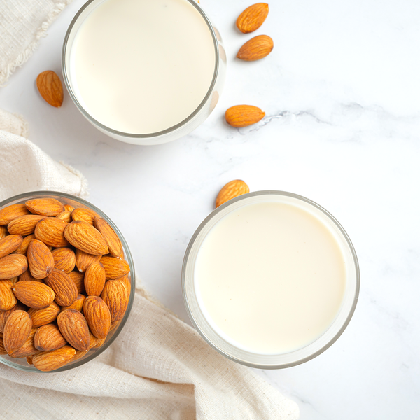 a small glass milk bottle filled with almond milk surrounded by raw almonds