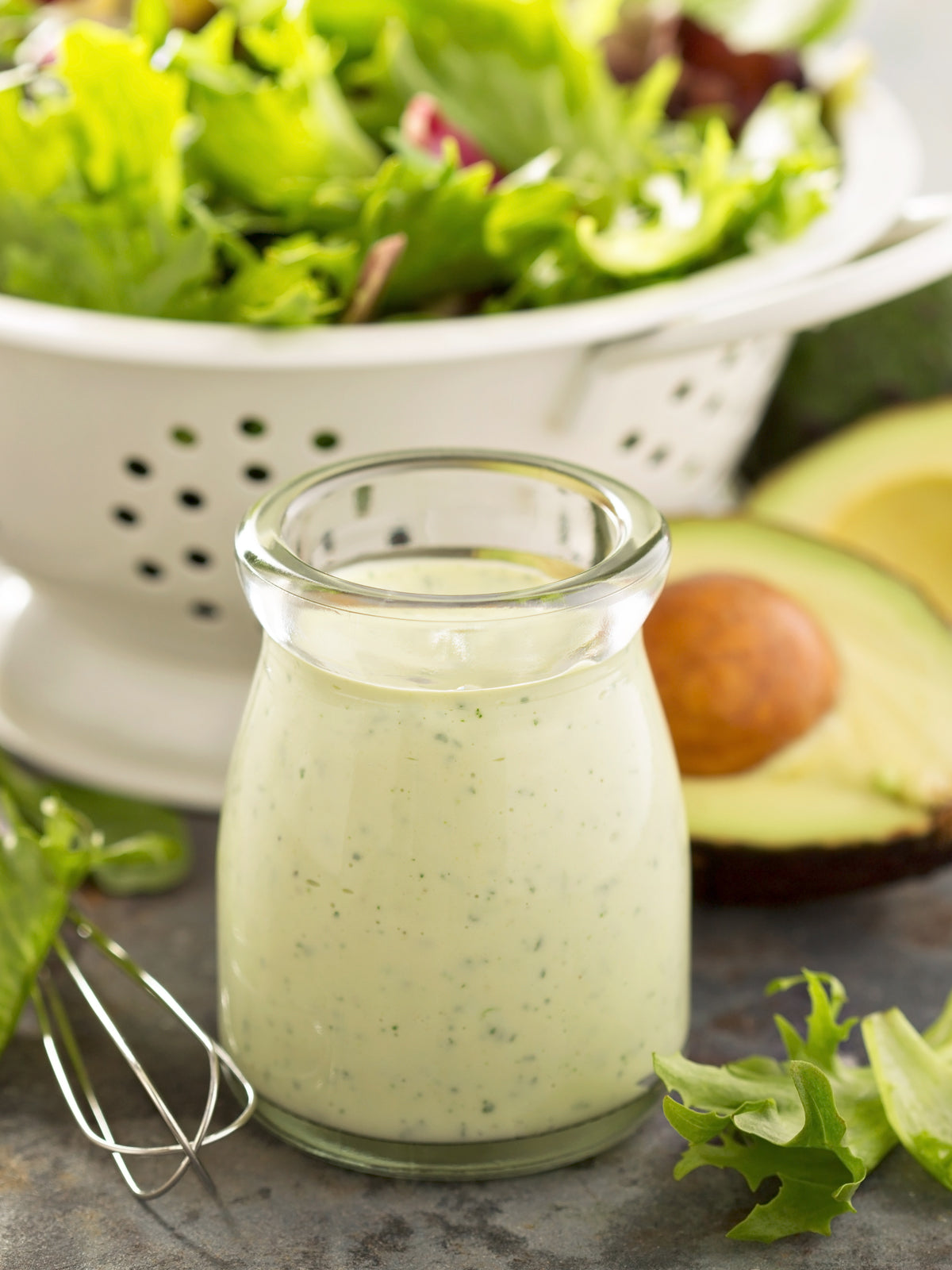 prepared salad in a colander with a bottle of avocado lime salad dressing