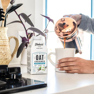 a woman pouring coffee from a French press coffee maker using Elmhurst French Vanilla Oat Milk Creamer